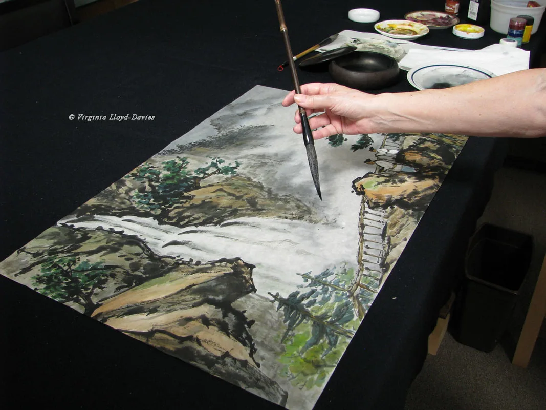 Hand holding brush above painting of waterfall